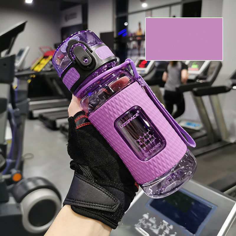 Purple water bottle with a black grip held by a person in a gym setting