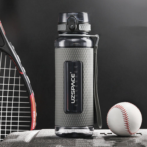 Gray water bottle with UZSPACE branding next to a tennis racket and baseball on a dark background